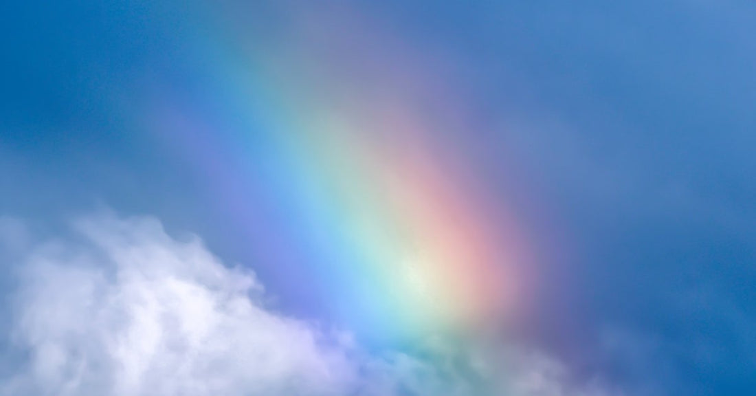 A vivid rainbow blending into a blue sky above soft white clouds, with faint color bands across the open sky.