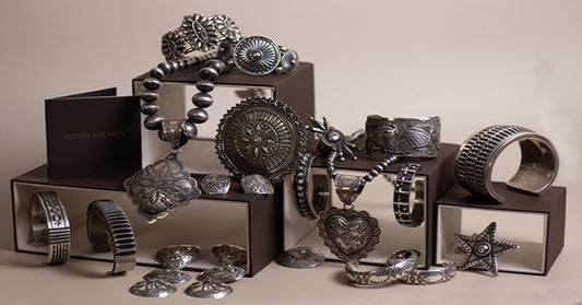 A collection of silver-toned bracelets, rings, pendants, and concho jewelry arranged on mirrored display boxes.