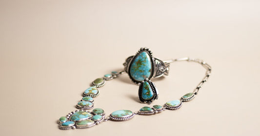 A turquoise jewelry set with a necklace, ring, and dangling earring arranged on a beige cloth surface.