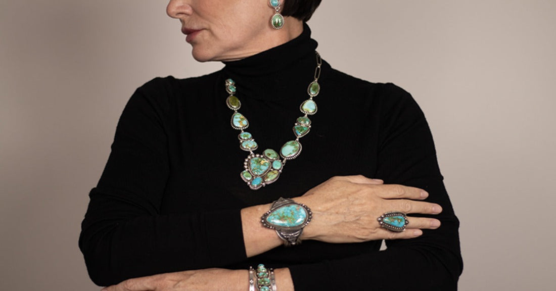 A person wearing a black turtleneck and turquoise jewelry, including a necklace, earrings, bracelets, and a ring.